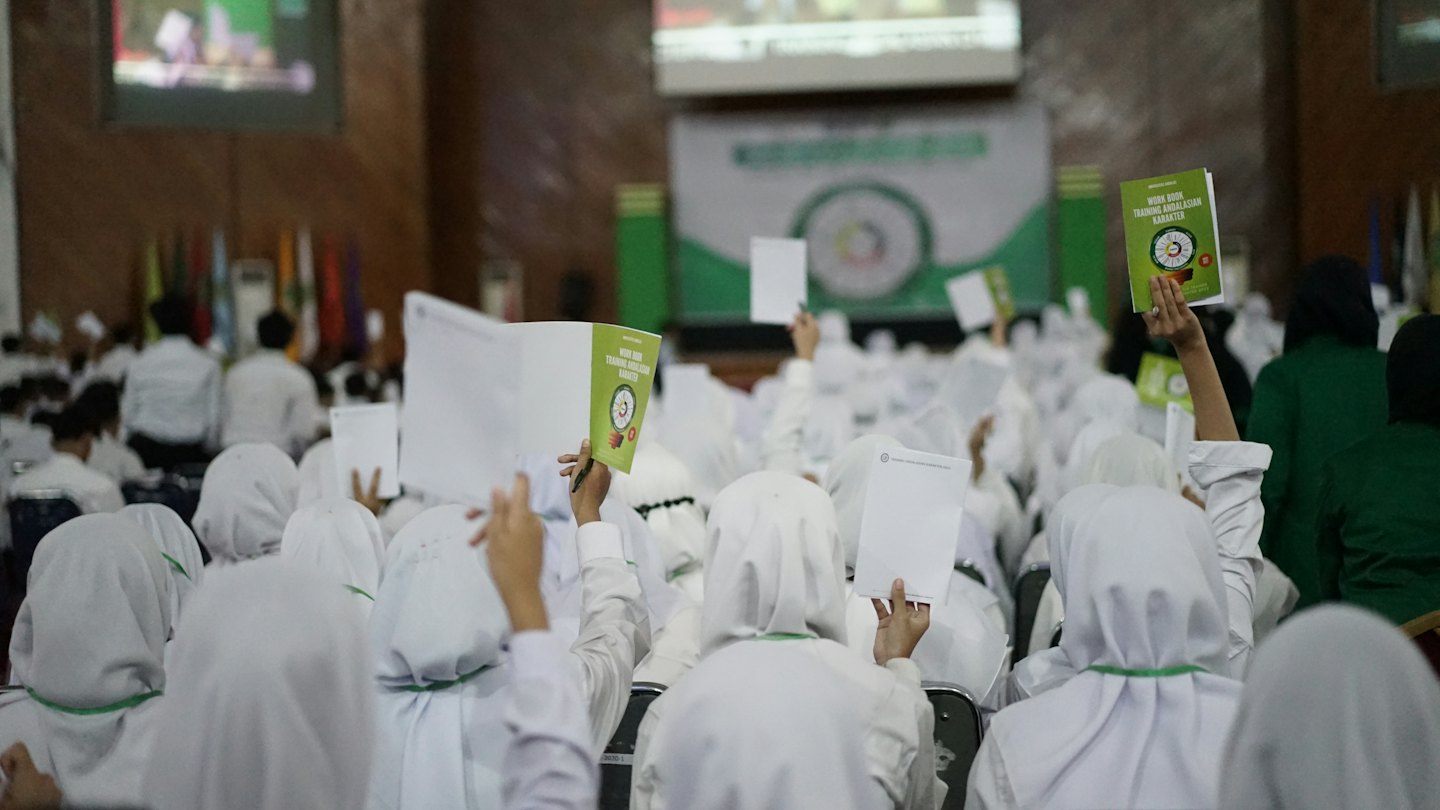 Attendees in a conference hall holding up instructional materials.