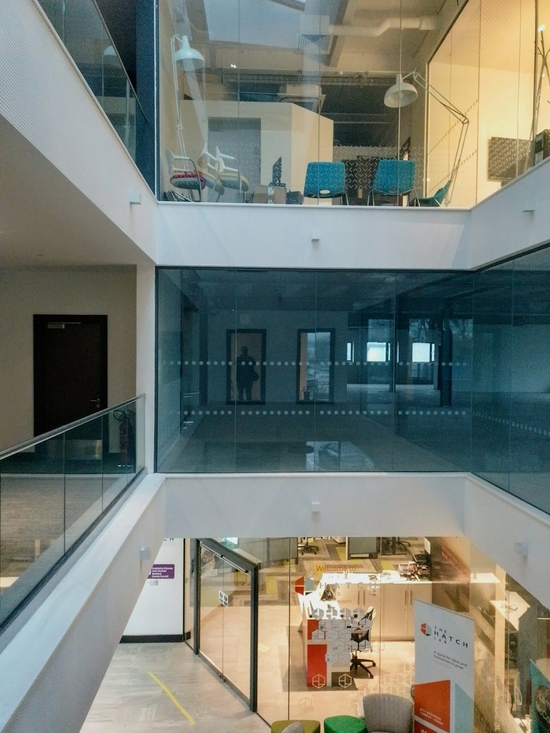 Modern office building atrium with glass walls and colorful chairs.