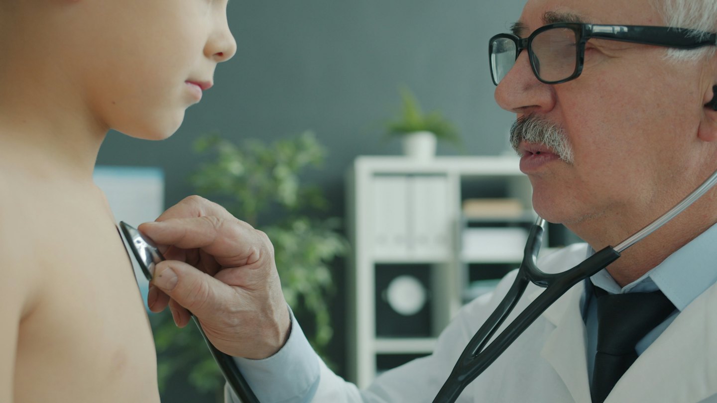 Doctor examines young boy with a stethoscope in a clinic.